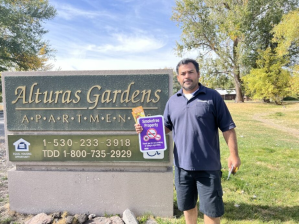 A person holding a no smoking sign in front of an apartment complex sign.